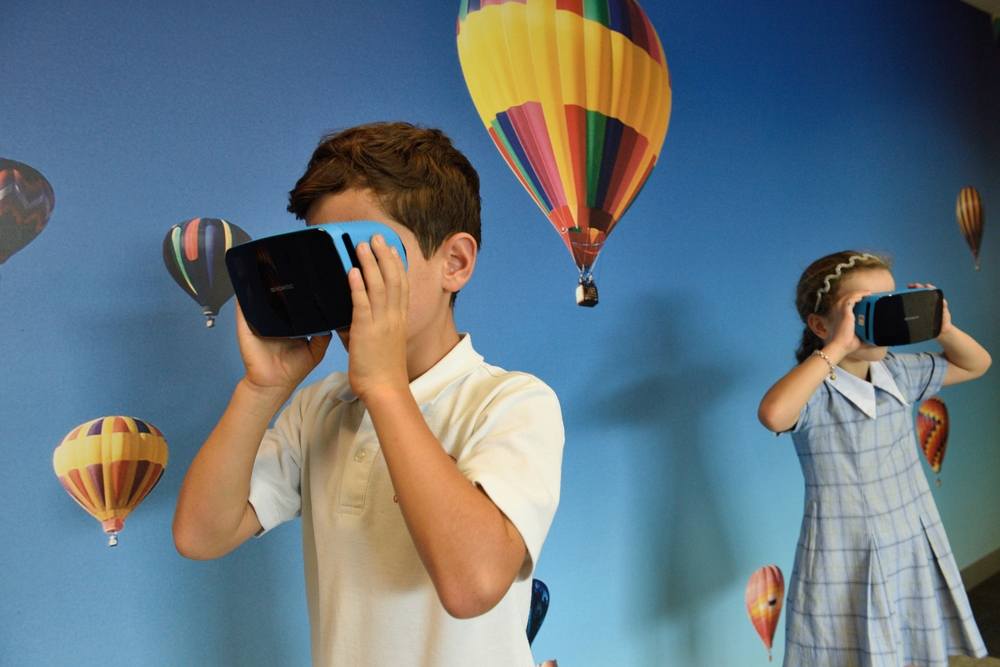 Two children in VR headsets watch hot-air balloons in the sky